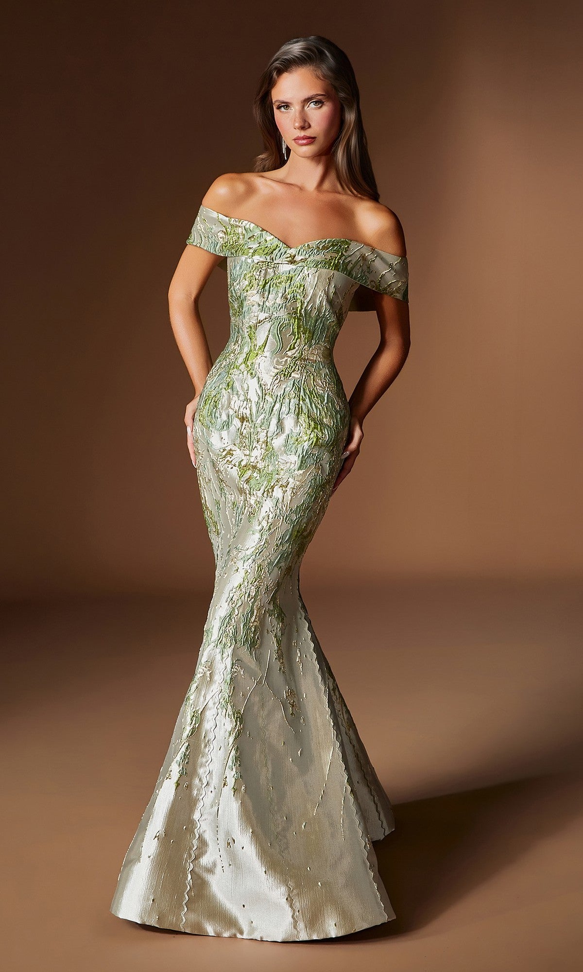 A woman poses against a plain brown backdrop wearing the Ladivine CD0107, an off-the-shoulder long formal dress in metallic green and silver jacquard with a fitted mermaid silhouette.